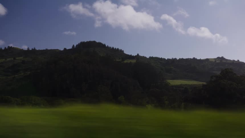 A scenic drive through a verdant countryside, revealing rolling green hills and forests under a sunny blue sky