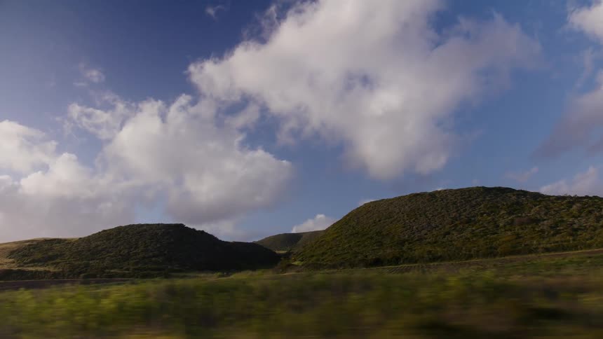 A scenic drive past rolling green hills and lush countryside under a beautiful blue sky with fluffy white clouds