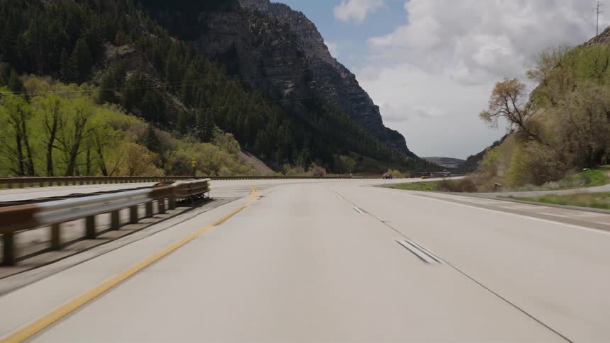 A point-of-view shot driving down a winding highway through a scenic mountain canyon under a partly cloudy sky