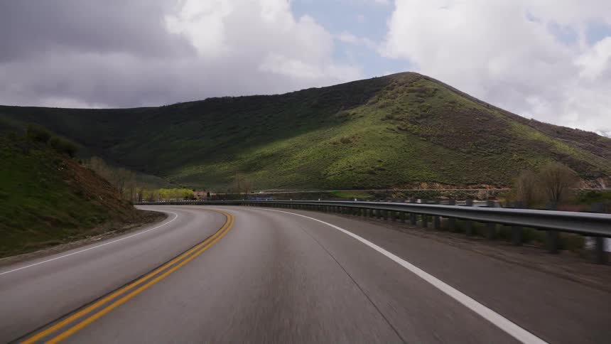 A red semi-truck passes by a car driving down a winding mountain highway with a snow-capped mountain in the distance