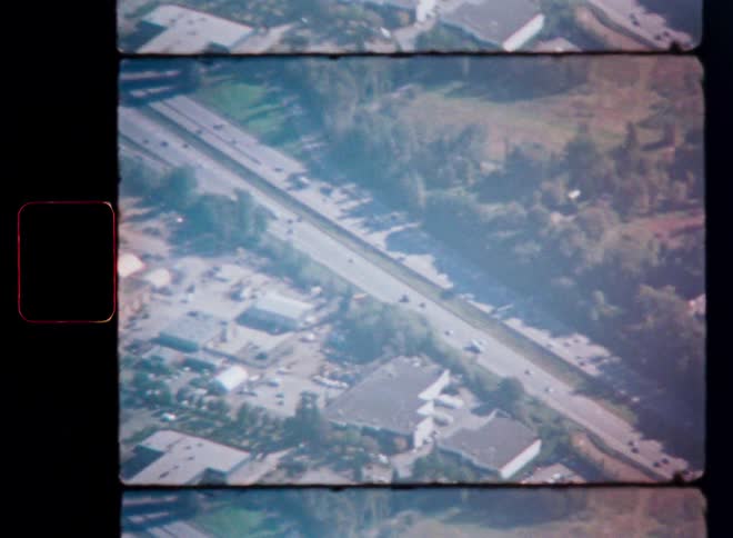 Vintage aerial film footage shows a busy highway cutting through a green, forested landscape, captured from above