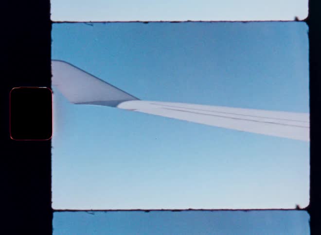 Vintage 8mm film captures the view from an airplane window, showing the wing and engine soaring through the blue sky high above the clouds