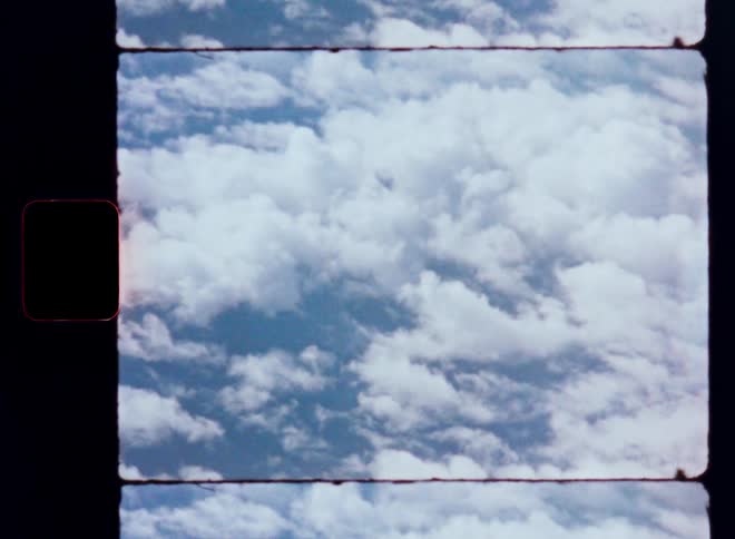 Vintage 8mm film scan of a static shot of a blue sky filled with fluffy white clouds
