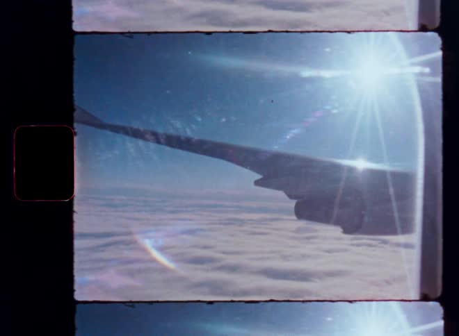 An 8mm film scan shows a dreamy view from an airplane window, with the wing soaring over endless clouds under a bright, flaring sun