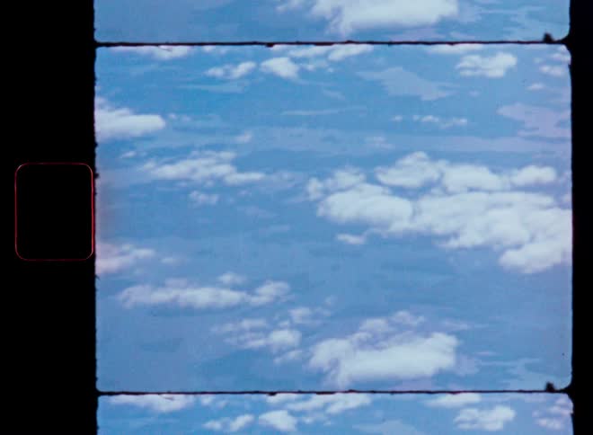 A vintage aerial view from an airplane window shows clouds scattered across a blue sky with the earth visible below