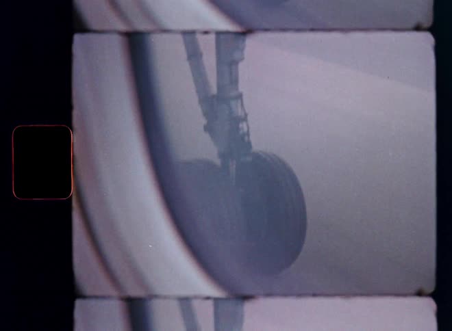 Vintage 8mm film captures an abstract, blurry close-up of an airplane's landing gear taxiing on the runway