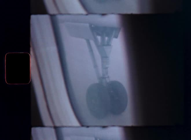 An airplane's landing gear rolls on the tarmac in this vintage 8mm film clip with visible sprocket holes and frame lines