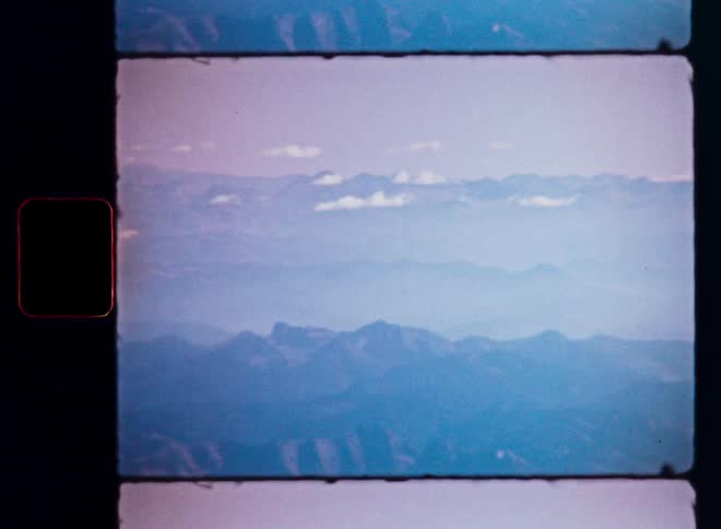 A still frame from a vintage Super 8 film shows a beautiful aerial shot of hazy blue mountains and clouds