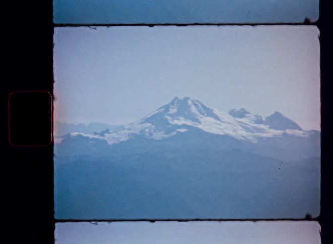 Vintage 8mm film captures the hazy, majestic view of a snow-capped mountain range from an airplane window