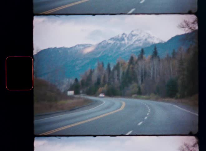Nostalgic Super 8 film view of a car driving on a scenic road towards snow-capped mountains