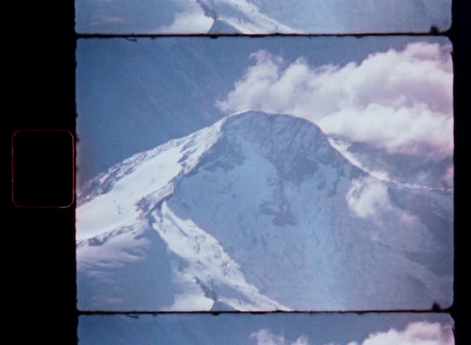 Close-up of a snow-covered mountain peak with passing clouds, scanned from vintage 8mm film