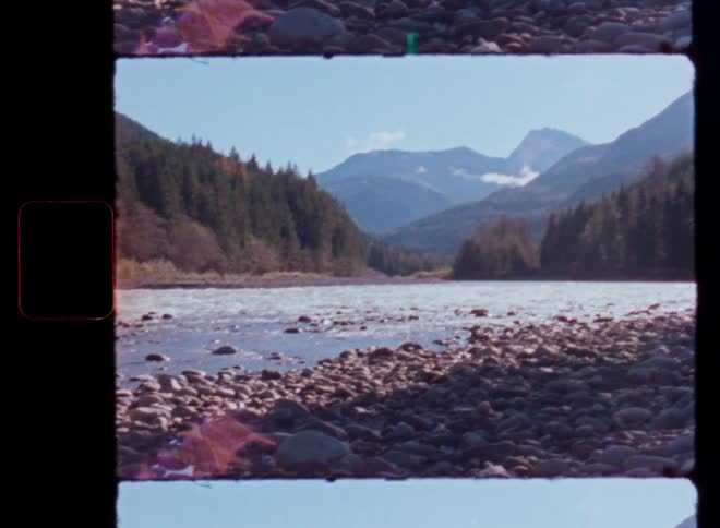 Super 8 footage shows a serene river flowing through a rocky valley with forested mountains in the background