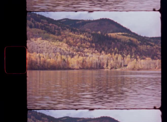 A vintage film shot captures a serene mountain lake reflecting the vibrant colors of the autumn forest