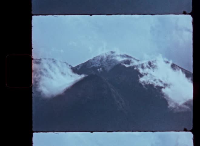 Vintage film footage captures clouds moving across majestic, snow-capped mountain peaks