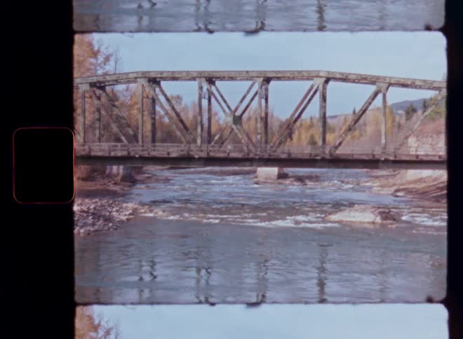 Authentic Super 8mm film shows a picturesque scene of a river flowing under a truss bridge during autumn