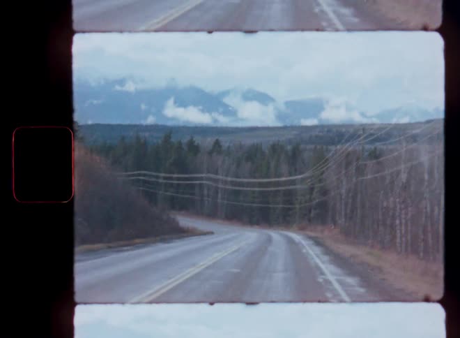 Vintage Super 8 film captures a drive down a winding road towards cloudy, snow-capped mountains