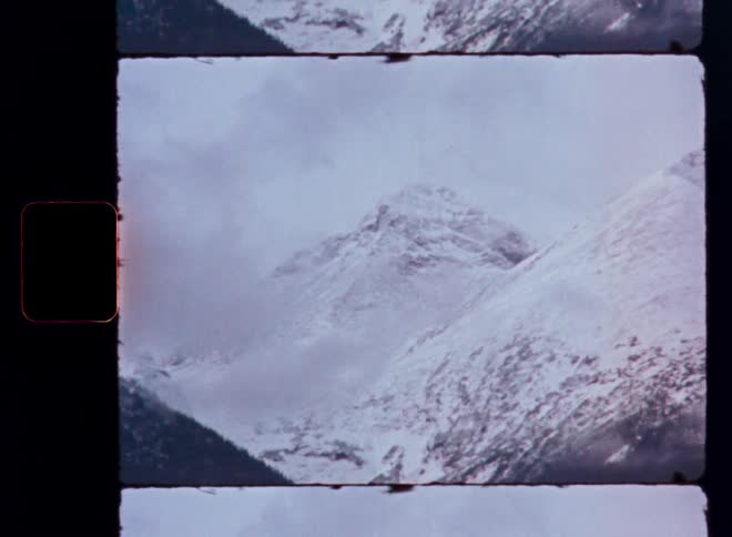 Archival film scan shows a majestic snow-capped mountain peak peeking through the clouds