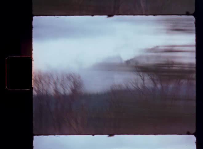 A vintage film view from a moving vehicle shows blurry trees passing by with foggy mountains in the distance