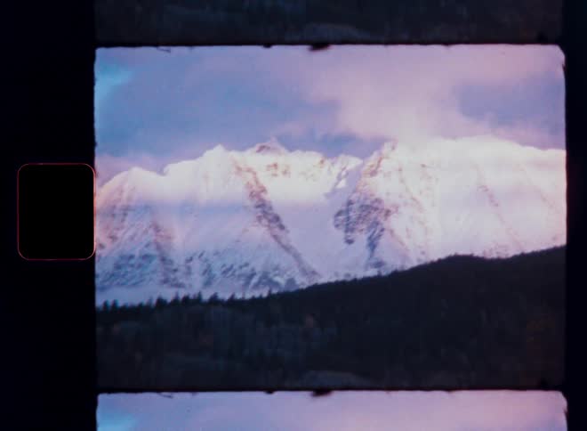 A scenic view of a majestic snow-capped mountain range with moving clouds is captured on vintage Super 8 film
