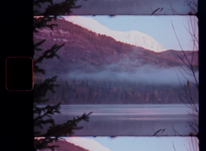 A vintage film-style shot captures a serene mountain lake at dawn with low-lying fog and snowy peaks, presented in a mirrored, split-screen effect