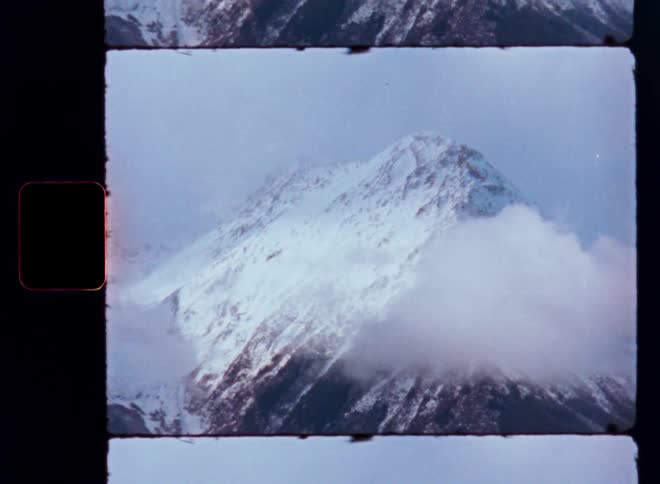Vintage Super 8mm footage captures a majestic snow-capped Himalayan mountain peak emerging from the clouds