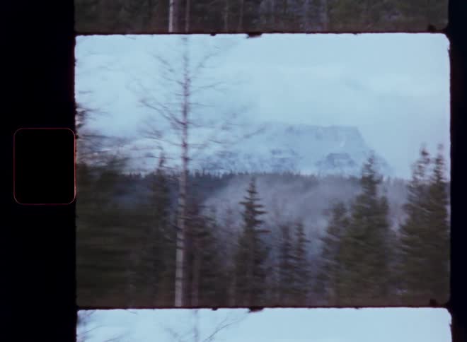 Vintage 8mm film of a snowy mountain and forest landscape viewed from a moving vehicle