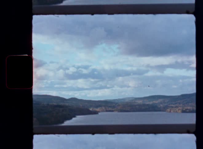 A vintage film strip shows a scenic view of a lake and autumn hills from a bridge on a cloudy day