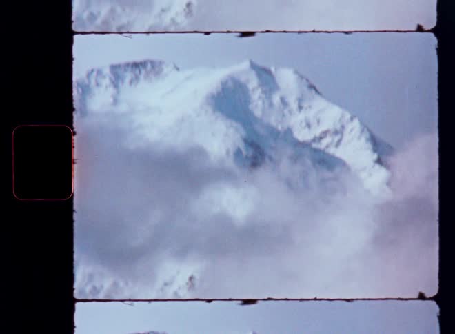 A vintage 8mm film shot of a snowy mountain peak emerging through a layer of thick clouds