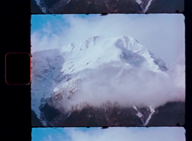 Authentic 8mm film captures the serene beauty of a snowy mountain range shrouded in mist