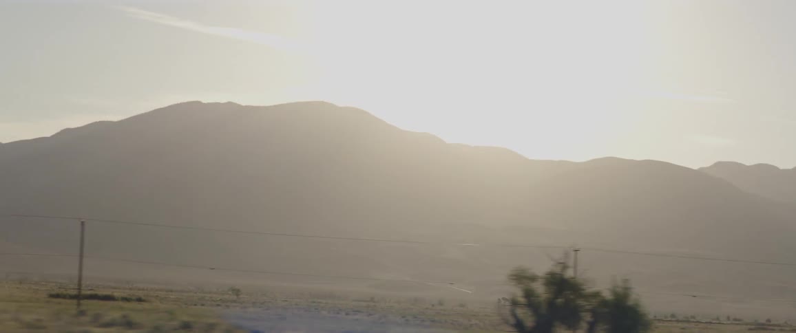 A tranquil, hazy view of a mountain landscape passing by from the window of a moving vehicle at sunrise