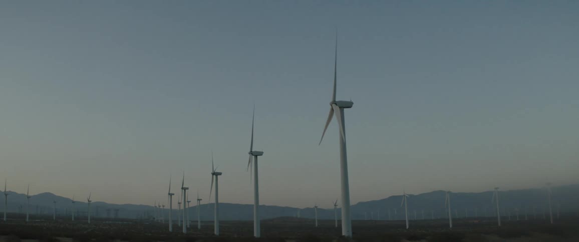 Rows of wind turbines spin slowly across a vast desert landscape at dusk