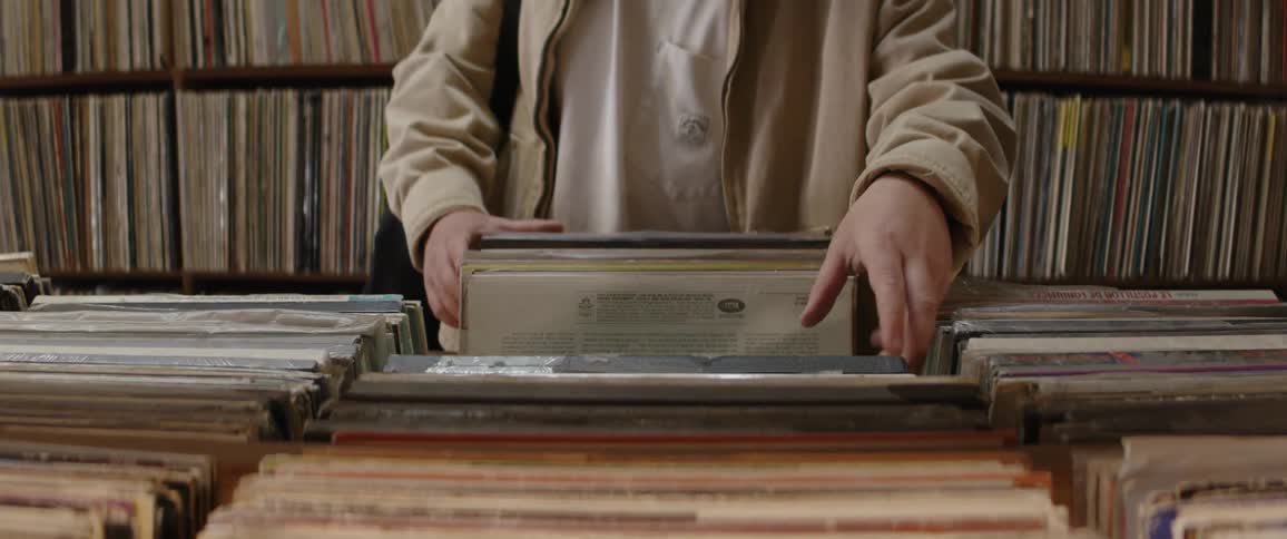 A person browses through a crate of classic vinyl LPs in a vintage record store