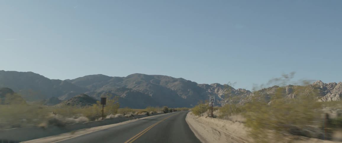 A scenic POV drive along a winding desert road surrounded by arid shrubs and rocky mountains under a clear sky