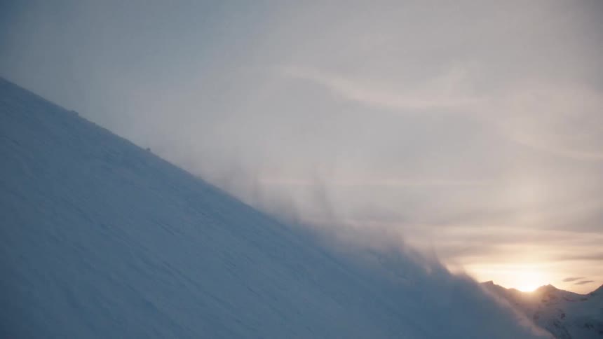 Dramatic slow motion of a skier carving through fresh powder down a steep mountain face at sunset