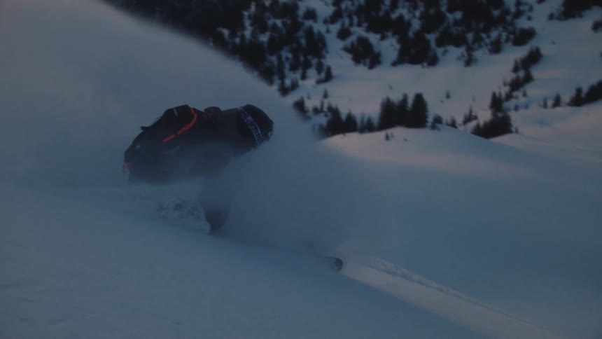 A skier gracefully carves through fresh powder on a snowy mountain as the sun sets in the background, captured in stunning slow motion