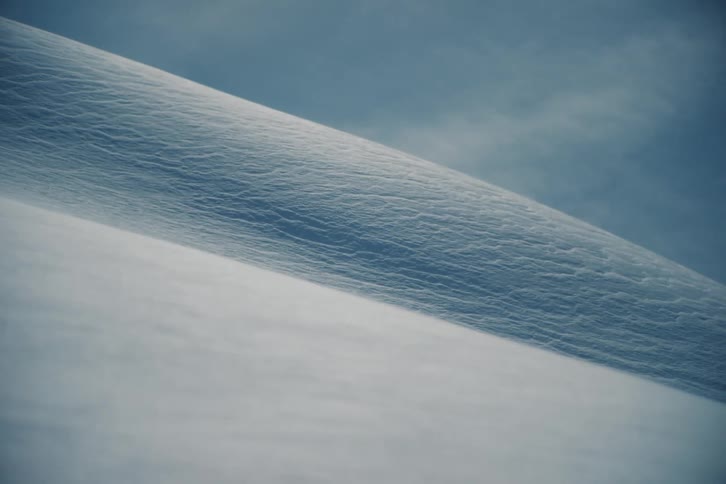 Wind blows fine snow across a serene and abstract winter landscape in a minimalist close-up