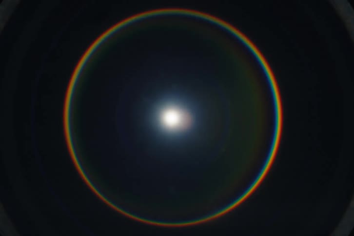 A vibrant rainbow-colored circular lens flare expands and contracts against a dark background