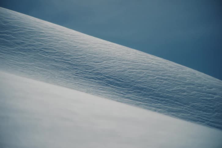 A cinemagraph shows a close-up of fine snow blowing across a textured, frozen landscape in a minimalist composition