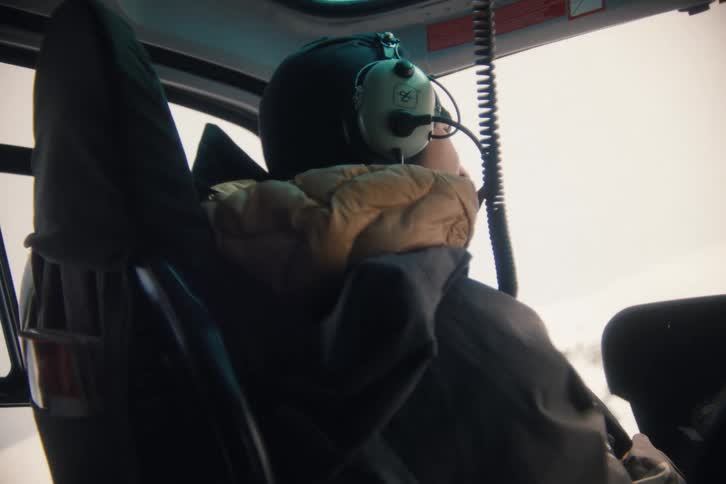 A person in a helicopter enjoys the view while flying over a vast, snow-covered landscape