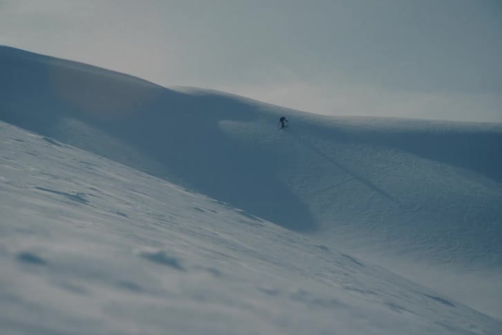 A lone backcountry skier treks up a vast, windswept snowy mountain in an epic winter landscape