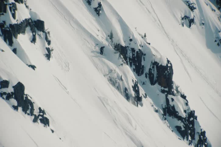 An expert skier carves down a vast and rugged snow-covered mountain, leaving fresh tracks in the powder