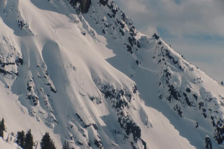 Wide shot of an expert skier descending a massive, untouched snowy mountain in the backcountry
