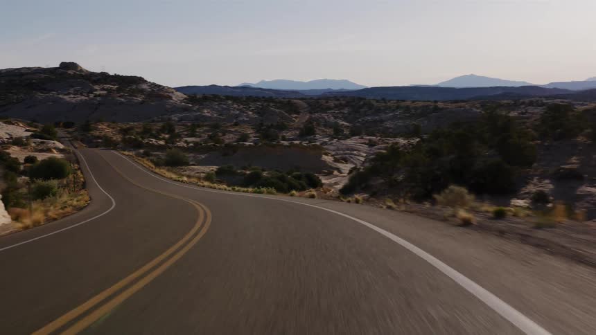 A point-of-view drive on a winding road through a scenic desert canyon landscape under a clear sky