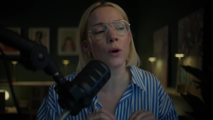 A blonde woman in glasses passionately records a podcast in her stylish, dimly lit home studio at night