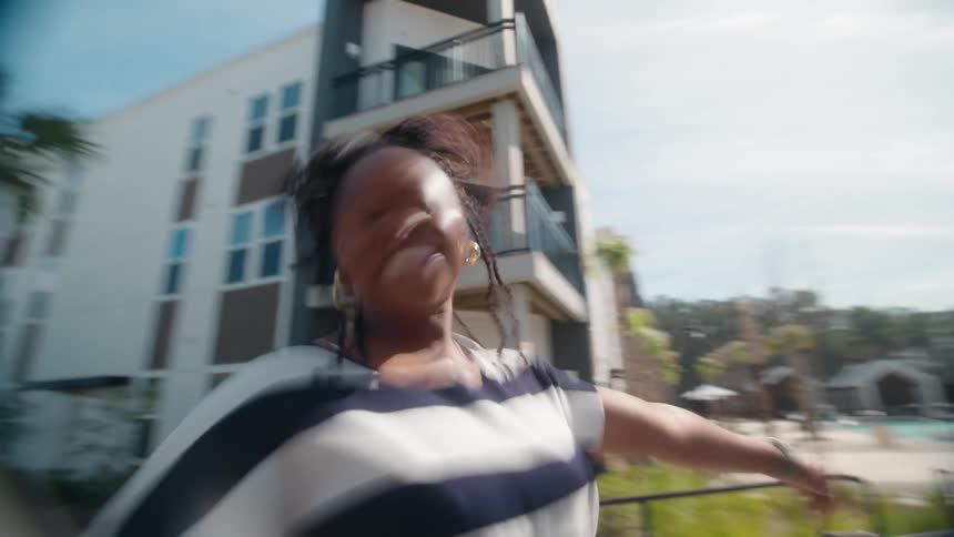 Energetic friends dance with joyful abandon in a blurry, slow-motion shot outside a modern apartment building on a sunny day