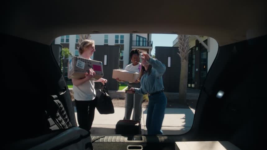 POV from inside a car trunk as three happy friends unload their belongings on move-in day before closing the trunk in slow motion