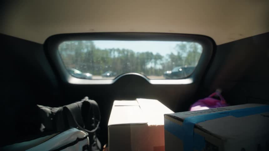 A point-of-view shot from the trunk of a car filled with moving boxes driving through a suburban neighborhood