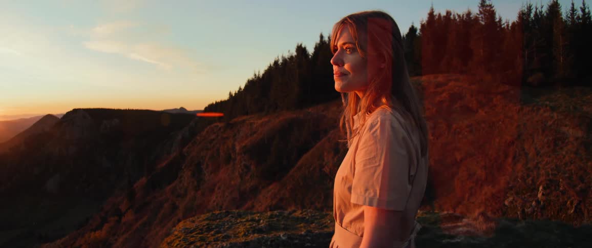 A cinematic slow-motion shot reveals a woman holding a flaming torch while she watches the beautiful golden sunset from a mountain vista