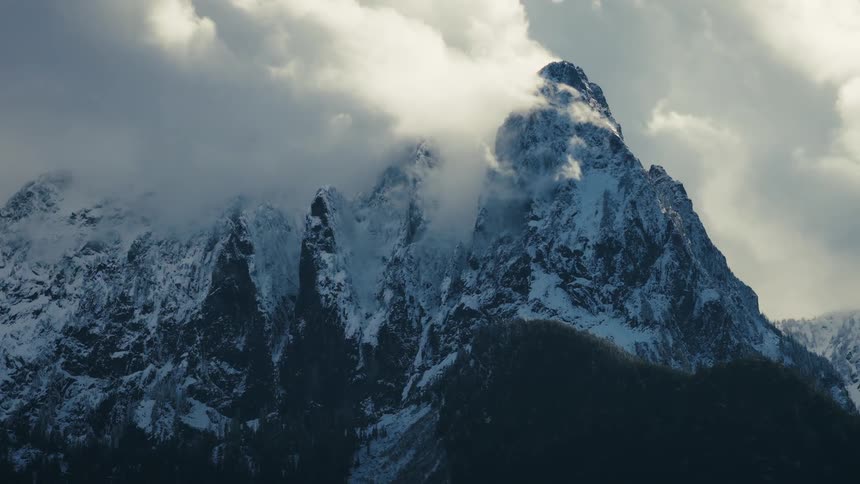 Dramatic clouds swirl around a majestic, snow-capped mountain peak