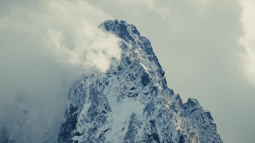 A dramatic close-up of a snow-covered mountain peak shrouded in swirling clouds